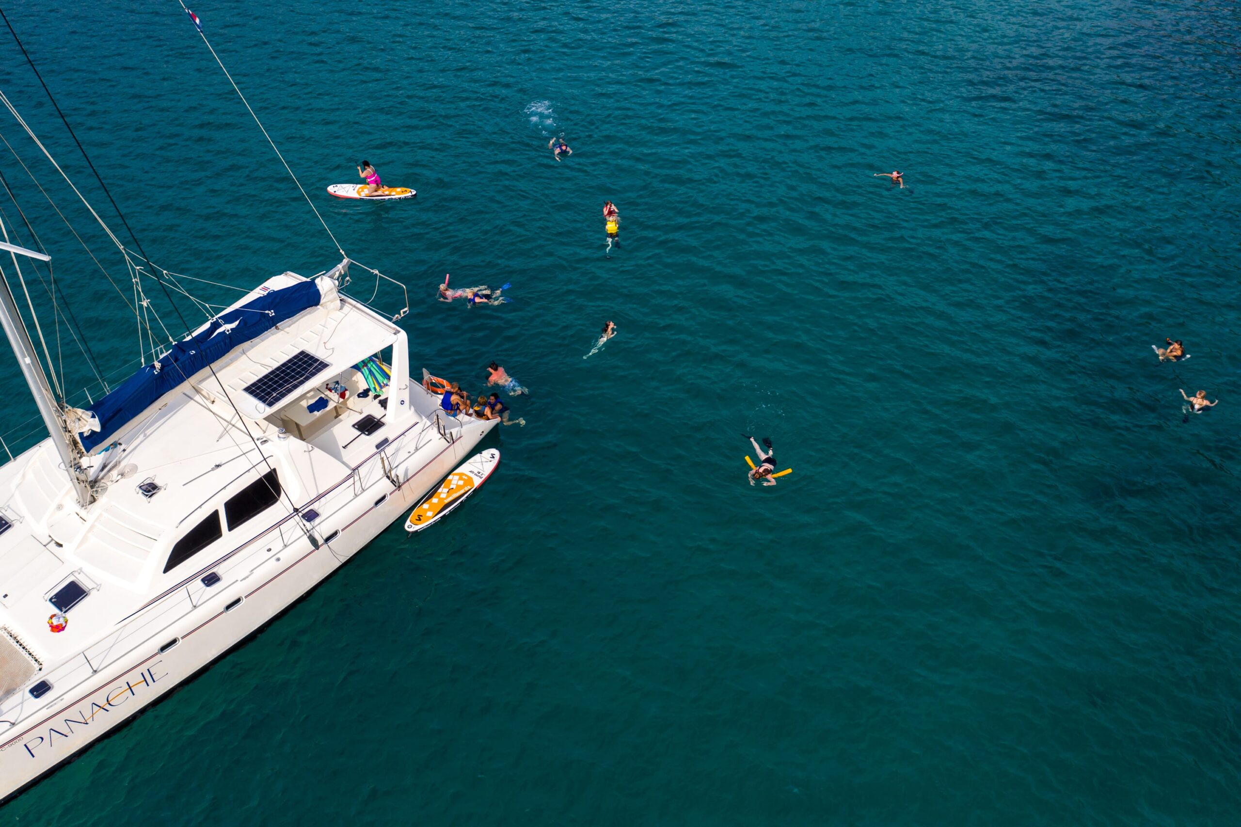 People swimming and relaxing near a catamaran in clear turquoise waters.