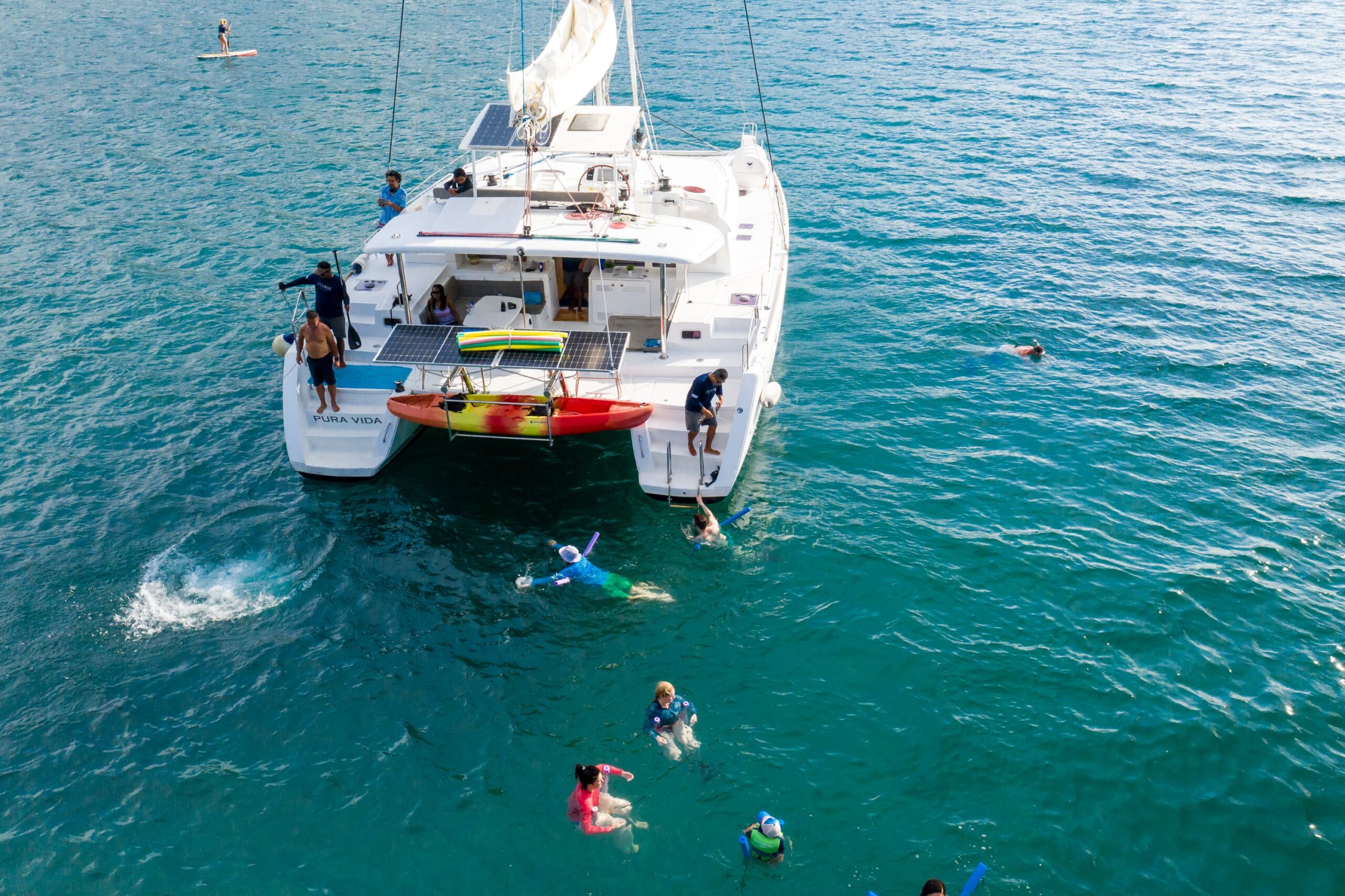 A catamaran anchored in turquoise waters with people swimming and snorkeling nearby.